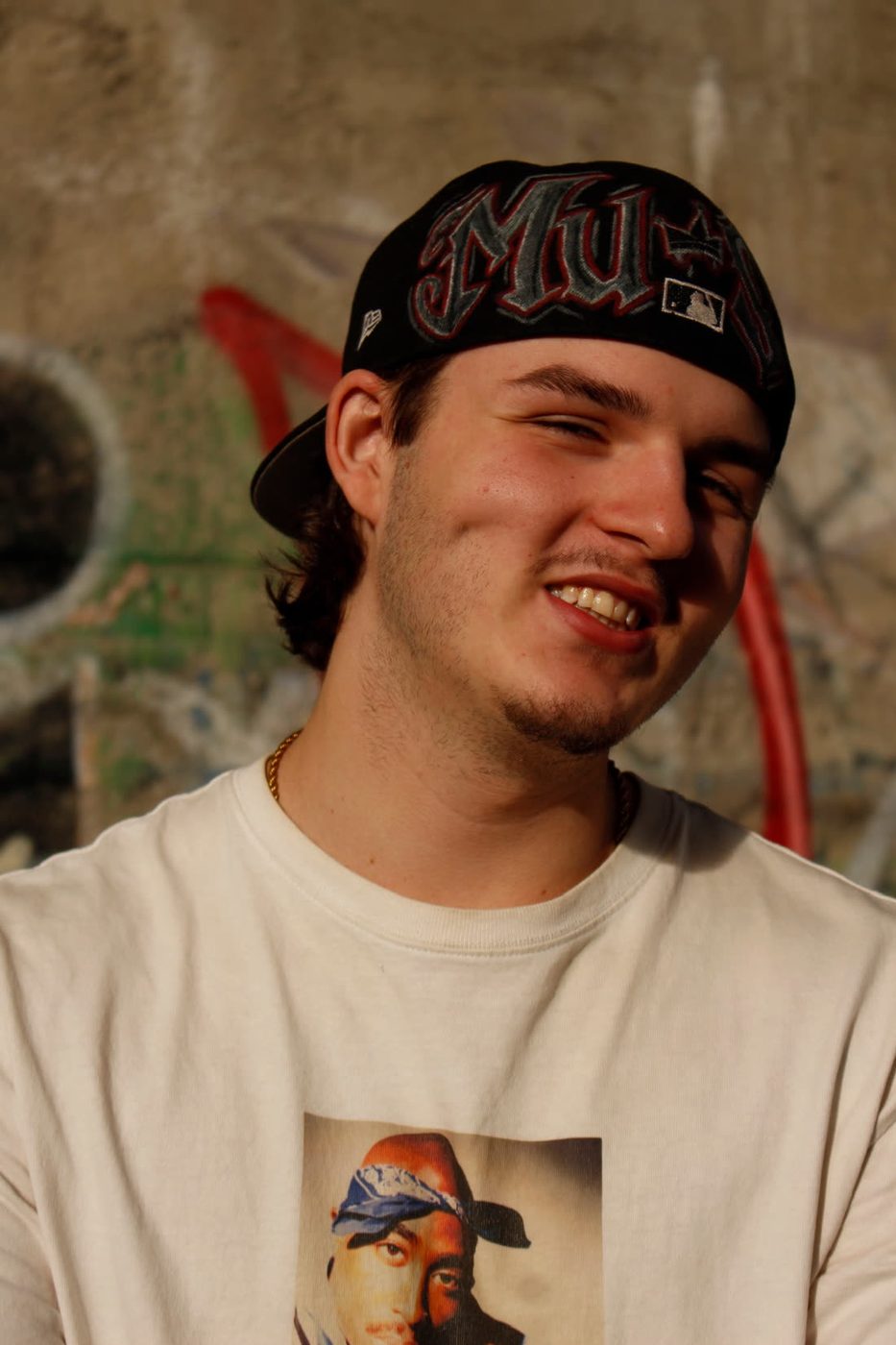 Must, portrait souriant devant un mur de graffitis